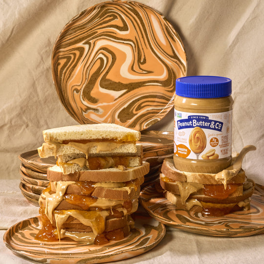 Peanut butter and jelly sandwiches on marbled plates with a jar of peanut butter in the background.