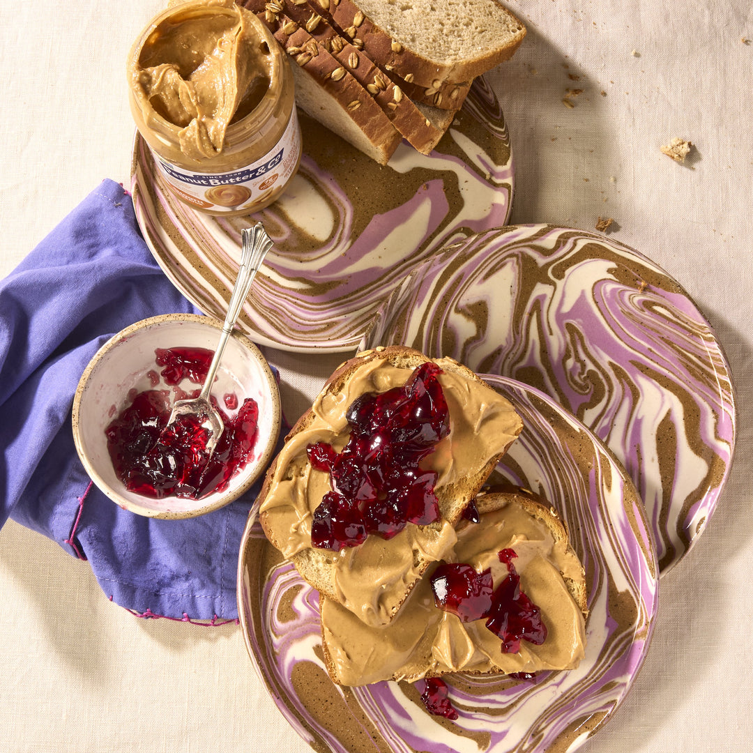 Two slices of bread with peanut butter and jelly on a marbled plate, next to a jar of peanut butter and a bowl of jelly.
