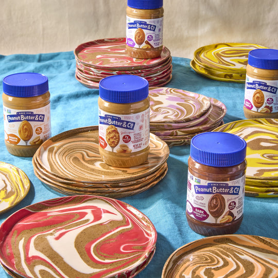 Peanut butter jars with blue lids on a table with colorful swirled plates.