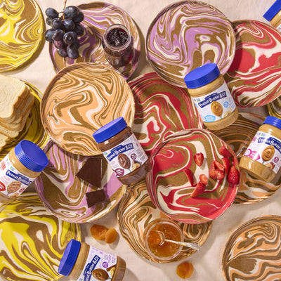 Marbled dessert plates with peanut butter jars and fruit on a beige background