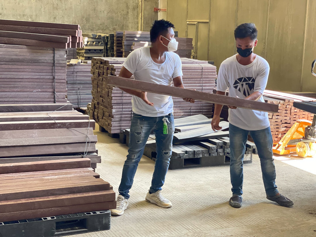Two men lift and look at a beam made of re-used plastics, part of a Plastic upcycling program in Davao, which is collecting and processing HDPE, PP, LDPE, and PET and turning plastic waste into useful products like benches, tables, and chairs