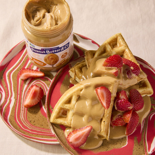 Waffles with peanut butter and strawberries on a plate next to a jar of peanut butter.